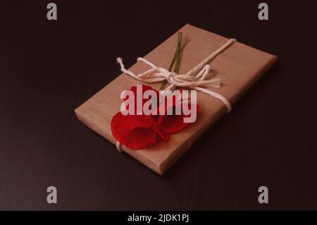 il regalo è avvolto in carta artigianale sulla parte superiore si trova un bouquet di papaveri rossi su uno sfondo scuro Foto Stock