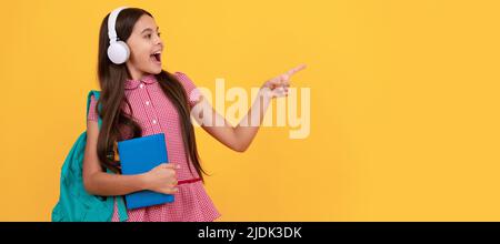 la ragazza teen della scuola stupita nelle cuffie punta il dito sullo spazio della copia, di nuovo alla scuola. Manifesto orizzontale isolato della studentessa della scuola. Intestazione banner Foto Stock