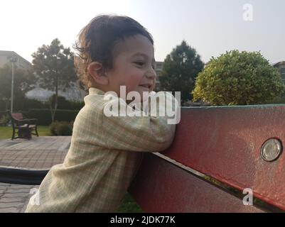 Carino ragazzino in piedi su una panca in un parco. Foto Stock