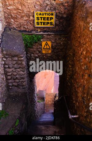 attenzione gradini ripidi in cima ai gradini del castello che scendono tra le pareti di pietra rosso scuro Foto Stock