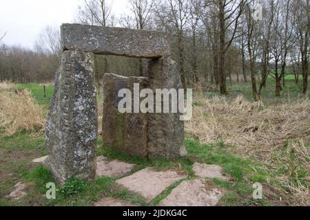 pietre in piedi formando un arco in un campo con alberi sullo sfondo e un cielo blu d'inverno Foto Stock