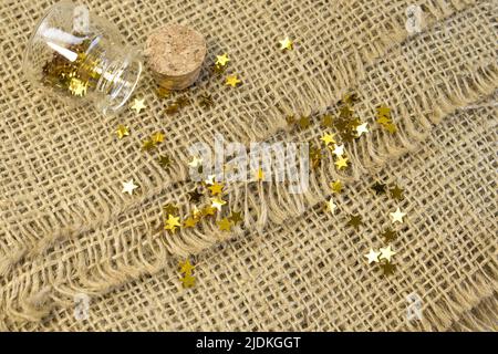 Paillettes tube stelle d'oro sparse brillano su tela ruvida sfondo testurizzato da vicino vista dall'alto Foto Stock