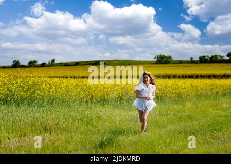 Bella ragazza sognante energica in un vestito bianco e un brillante brughiera Ucraina colorata scorre attraverso campi di colza gialli in fiore e verde spr Foto Stock