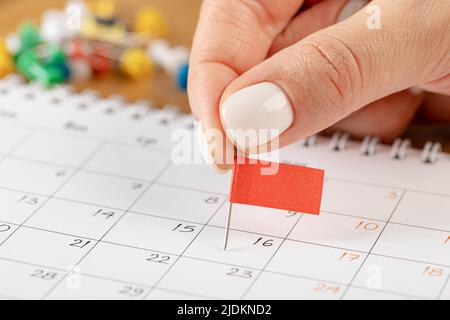 Calendario delle note di fissaggio a mani, anteprima con puntina rossa nel calendario per riunioni e promemoria appuntamento Foto Stock