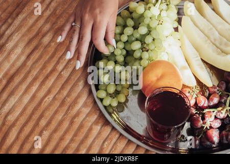 Vista dall'alto in basso di uva femmina che raccoglie da vassoio di frutta che si trova sul letto Foto Stock