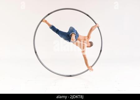 Fit maschio acrobat esecuzione di una gamba handspring su una ruota cyr mentre in movimento rotatorio su uno sfondo bianco con copyspace Foto Stock