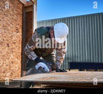 Carpentiere con sega circolare per il taglio del legno OSB. Uomo lavoratore edificio legno telaio casa. Concetto di carpenteria. Foto Stock