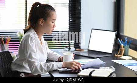 Donna d'affari asiatica che gestisce le operazioni aziendali, analizza i dati di commercio, piani di marketing presso la scrivania d'ufficio Foto Stock