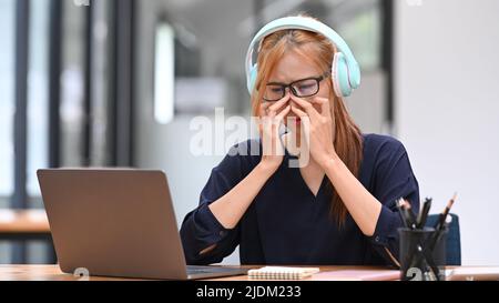 Stanco lavoratore di ufficio asiatico femminile che soffre di sintomi di visione sfocata dopo l'uso lungo del laptop, sente il problema di tensione occhio Foto Stock