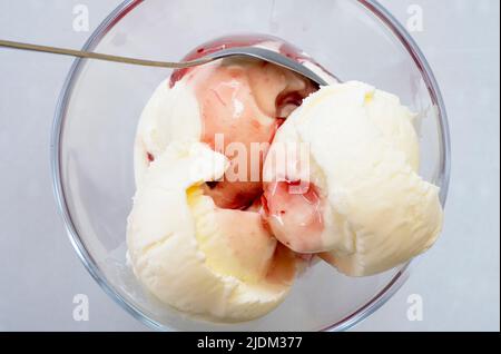 Tre palline di vaniglia di un gelato con sciroppo di fragola in un recipiente di vetro, vista dall'alto Foto Stock