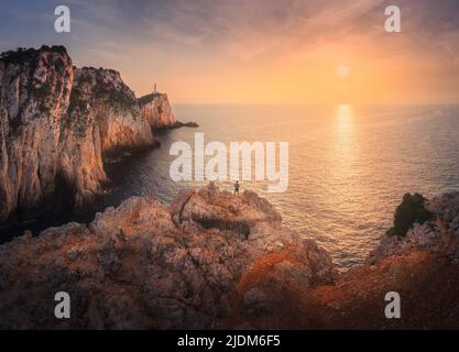 Veduta aerea dell'uomo sulla cima della montagna, faro, mare al tramonto Foto Stock