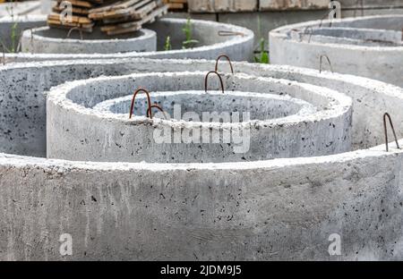 Anelli tondi in cemento armato in un cantiere. Prodotti in cemento armato per dispositivi di comunicazione sotterranea. Costruzione di cucire Foto Stock
