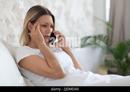 Signora carina infelice che ha una telefonata a letto Foto Stock