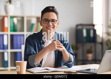 Ritratto di giovane imprenditore maschio in posa alla scrivania con laptop in ufficio Foto Stock