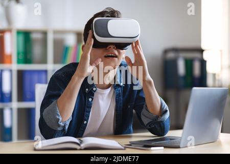 Giovane impiegato di ufficio maschile che utilizza occhiali VR mentre si siede alla scrivania Foto Stock