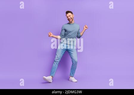 Foto di adorabile ragazzo fortunato indossare camicia grigia avendo divertimento danzare crescente pugni isolato viola sfondo di colore Foto Stock