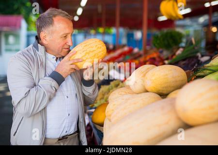 Uomo che sceglie i meloni nel negozio di frutta Foto Stock