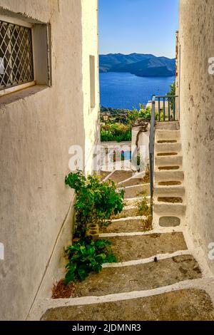 Vista tipica al tramonto nel piccolo villaggio greco di fronte al mare. Case imbiancate, vasi di fiori, colline, laguna, vigneti. Plaka città, isola di Milos, Grecia Foto Stock