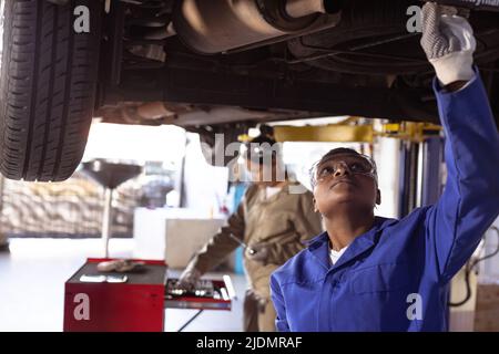 Saldatrici multirazziali per adulti di media età che utilizzano attrezzature durante la riparazione dell'auto su un ascensore in officina Foto Stock