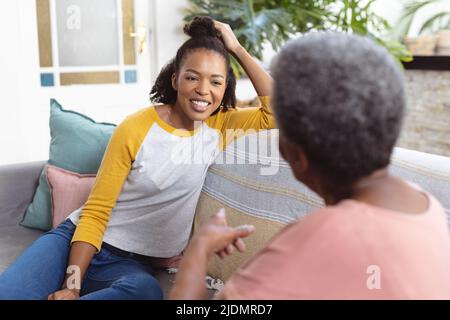 Sorridente giovane figlia afroamericana che guarda la madre anziana che parla mentre si siede sul divano Foto Stock