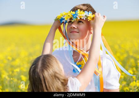 Sorella mette su fratello corona Ucraina con nastri, sullo sfondo di campi e cielo Foto Stock