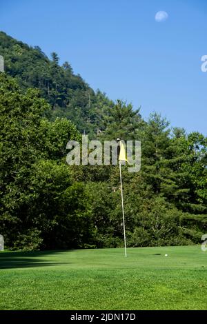 Bandiera e palla da golf si siedono sul verde, con una luna morbida nel cielo. Foto Stock