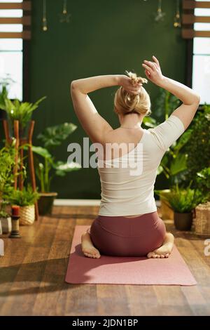 Visto da dietro la donna di mezza età nella casa verde che fa yoga. Foto Stock
