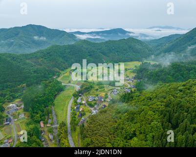 La nebbia al mattino presto si schiarisce su piccole fattorie in villaggio rurale di montagna Foto Stock