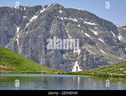 Un escursionista guarda fuori dalla riva di Drakolimni o Dragon Lake un lago alpino d'acqua dolce alto sul Monte Tymfi nelle montagne di Pindus del nord della Grecia Foto Stock