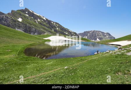 Un escursionista che si ferma dopo aver raggiunto Drakolimni o Dragon Lake un colle alpino sul Monte Tymfi nei Monti Pindus della Grecia settentrionale Foto Stock