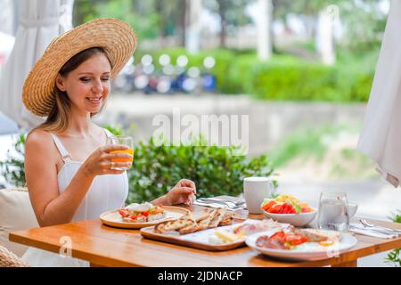 Giovane donna sorridente a colazione nel ristorante all'aperto dell'hotel. Vacanze estive Foto Stock