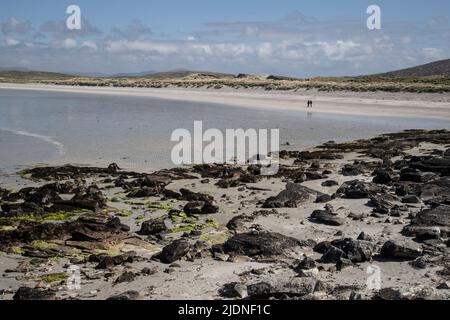 Una coppia in lontananza camminando oltre le rocce e le alghe sulle sabbie bianche di Clachan Sands in Uist del nord, Ebridi esterne Foto Stock