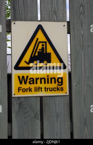 avvertenza i carrelli elevatori a forche sono indicati con lettere nere su uno sfondo giallo fissato a una recinzione di legno verde Foto Stock