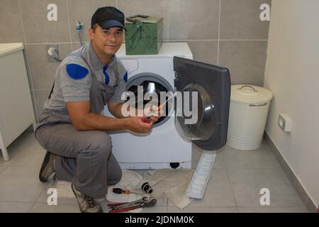 Immagine di un tecnico di elettrodomestici che sorride durante la riparazione di una lavatrice a casa di un cliente Foto Stock