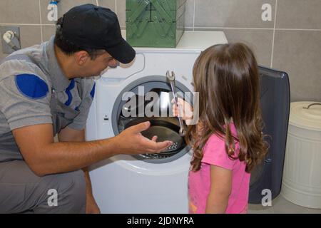 Immagine di un papà che ripara una lavatrice rotta con sua figlia aiutandolo con gli attrezzi Foto Stock