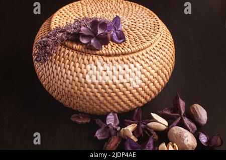 scatola di rattan in vimini rotonda sulla parte superiore con fiori secchi e lavanda su sfondo nero Foto Stock