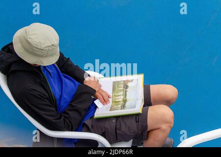 Vista dall'alto di un uomo seduto su una sedia che indossa un cappello che legge un libro Foto Stock