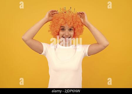 felice egoista divertente ragazza con look fantasia indossando parrucca capelli arancio e principessa corona, vincitore Foto Stock