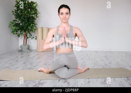 Ritratto di una giovane donna che medita in studio mentre si siede in una posizione di mezzo loto su un tappeto yoga. Foto Stock