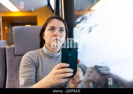 Il viaggiatore interessato filma paesaggi dietro il vetro in treno espresso Foto Stock