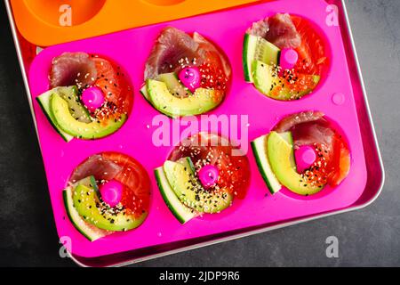 Preparazione del sushi a forma di ciambella in una muffa di silicone: Aggiunta di pesce fresco, uova di salmone, cetriolo e avocado a muffe di ciambelle Foto Stock