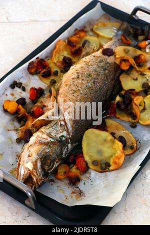 branzino atlantico al forno con patate, pomodoro e capperi, cucina mediterranea Foto Stock