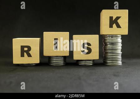 Successo in investimenti rischiosi e rischio di volatilità del mercato concetto. Blocchi di legno con monete e rischio di parola su sfondo nero scuro. Foto Stock