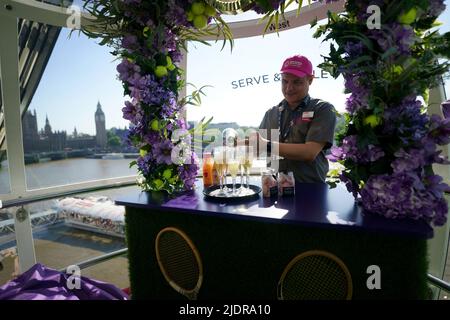 Un assistente serve champagne all'interno di una cialda sul London Eye lastminute.com, che è stato deocarted con un tema Wimbledon prima dell'inizio della competizione di tennis la prossima settimana. Data foto: Mercoledì 22 giugno 2022. Foto Stock