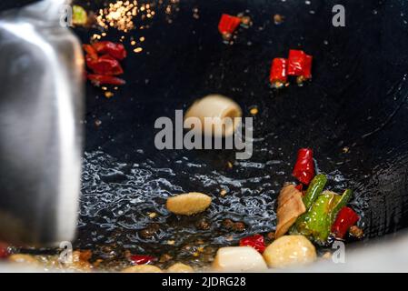 Chili e scalioni vengono fritti in un wok cinese Foto Stock