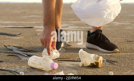 Uomo che pulisce spiaggia sabbiosa da plastica sulla riva del mare. Volontario raccogliere i rifiuti in un sacco rifiuti. Inquinamento da plastica oceanica. Natura problema ambientale Foto Stock