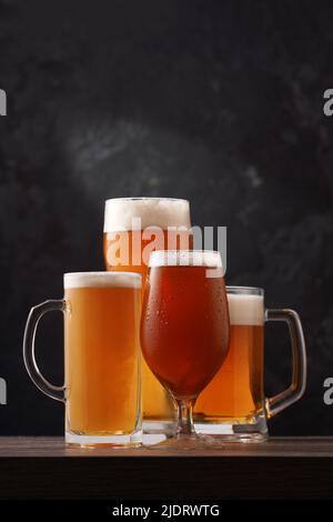 Quattro diversi bicchieri di birra su sfondo nero. Bevanda alcolica sullo sfondo del pub. Foto Stock