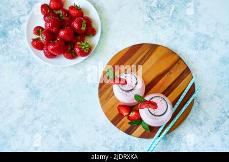 Frullato alla fragola o milkshake in vaso di vetro con frutti di bosco su fondo di cemento blu. Foto Stock
