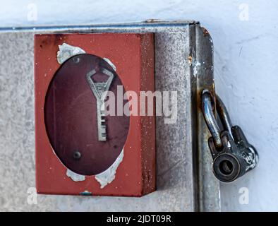 Un portachiavi rosso in vetro infrangente, usurato dalle intemperie, su una porta in metallo con lucchetto. Foto Stock