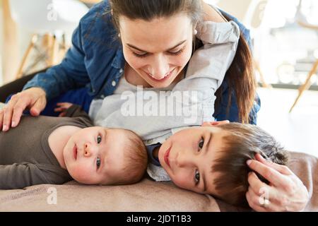 Una madre felice coccola con il bambino e il fratello grande nel soggiorno Foto Stock